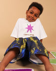 A young boy sitting on a beige floor wearing a white graphic t-shirt with a pink star and the text 'I AM A STAR.