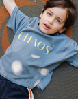Child wearing a blue t-shirt with 'CHAOS' printed on it, lying on a textured surface.