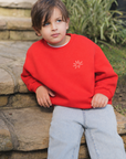 Child wearing a red sweatshirt with a logo, sitting on stone steps outdoors.