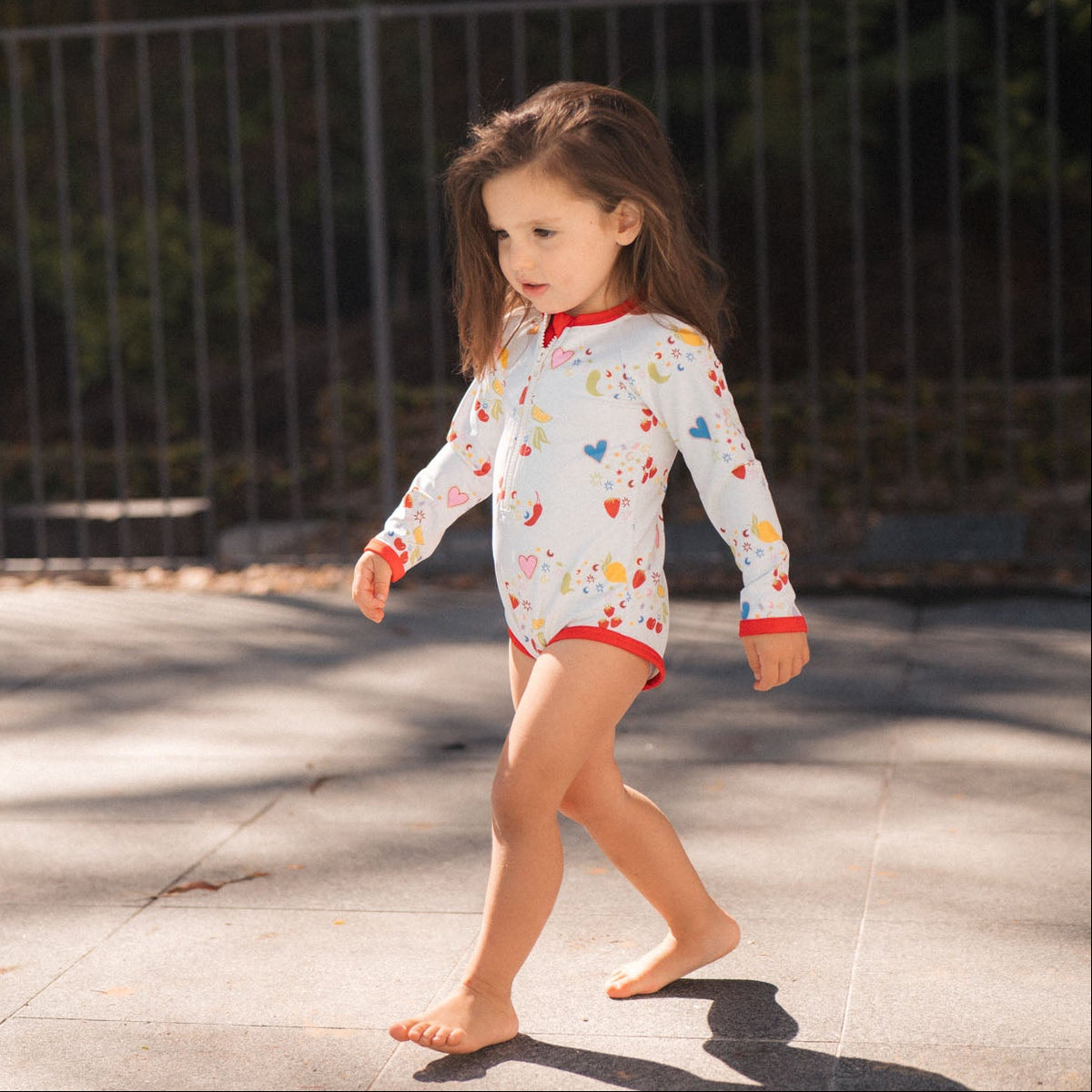 Young girl in a colorful swimsuit walking on a pavement.
