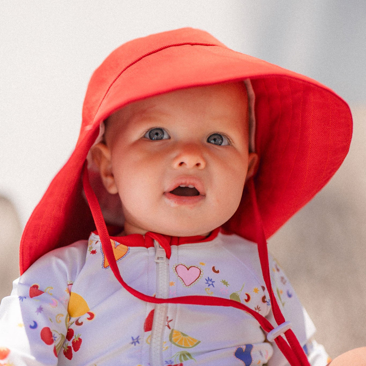 Baby wearing a colorful swimsuit and red sun hat with a blurred background