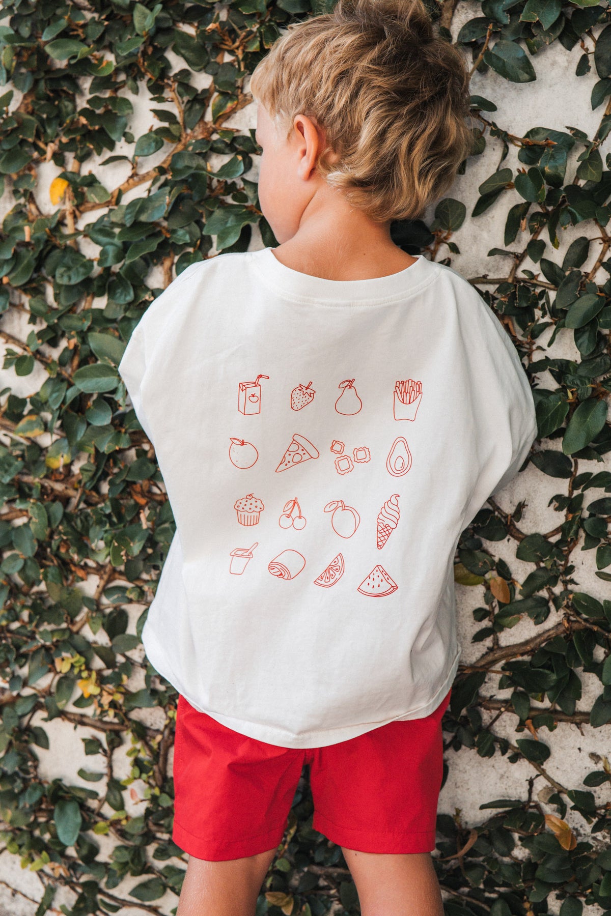 Child wearing a white t-shirt with red graphics against a leafy background
