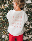 Child wearing a white t-shirt with red graphics against a leafy background