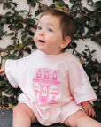 Baby sitting with a pink patisserie bodysuit against a leafy background.