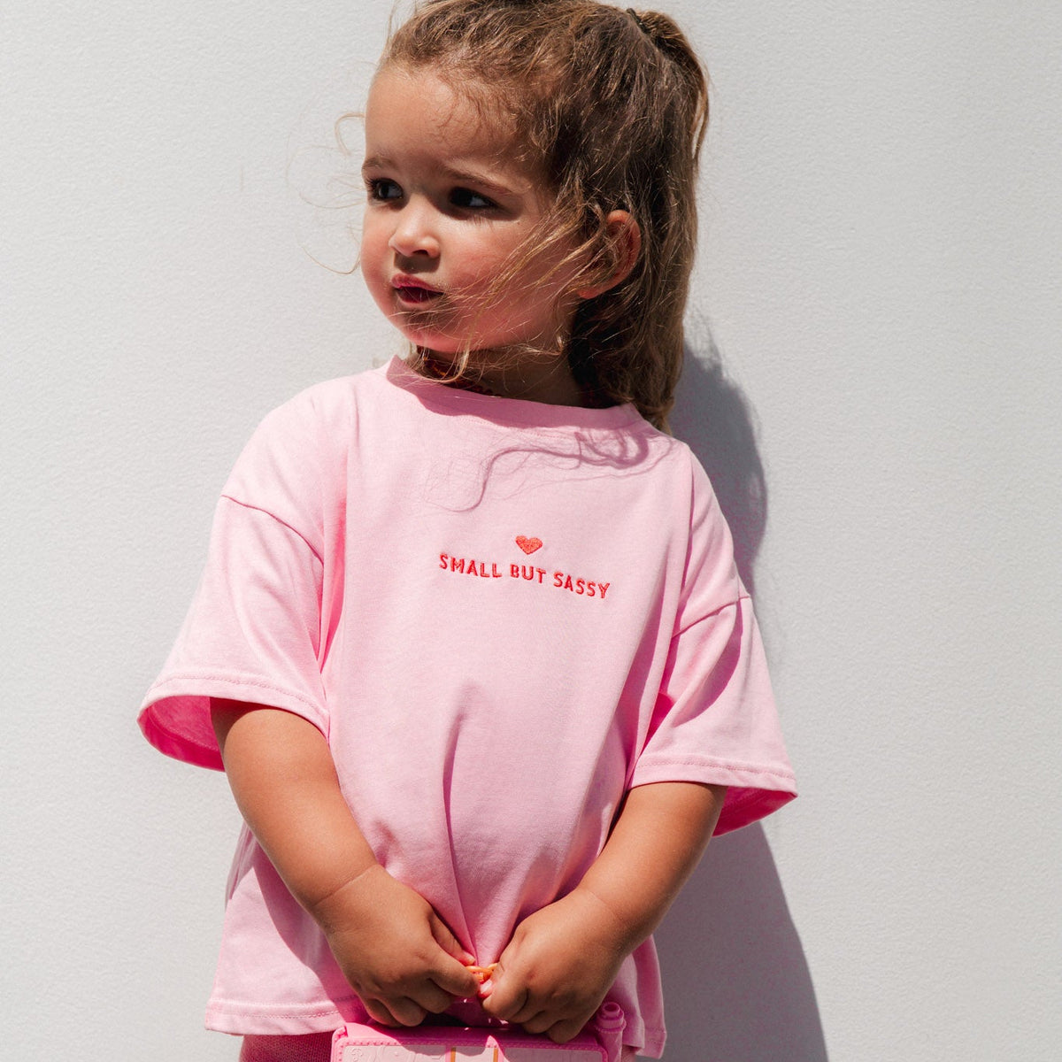  Child wearing small but sassy tee outdoors against a white wall.