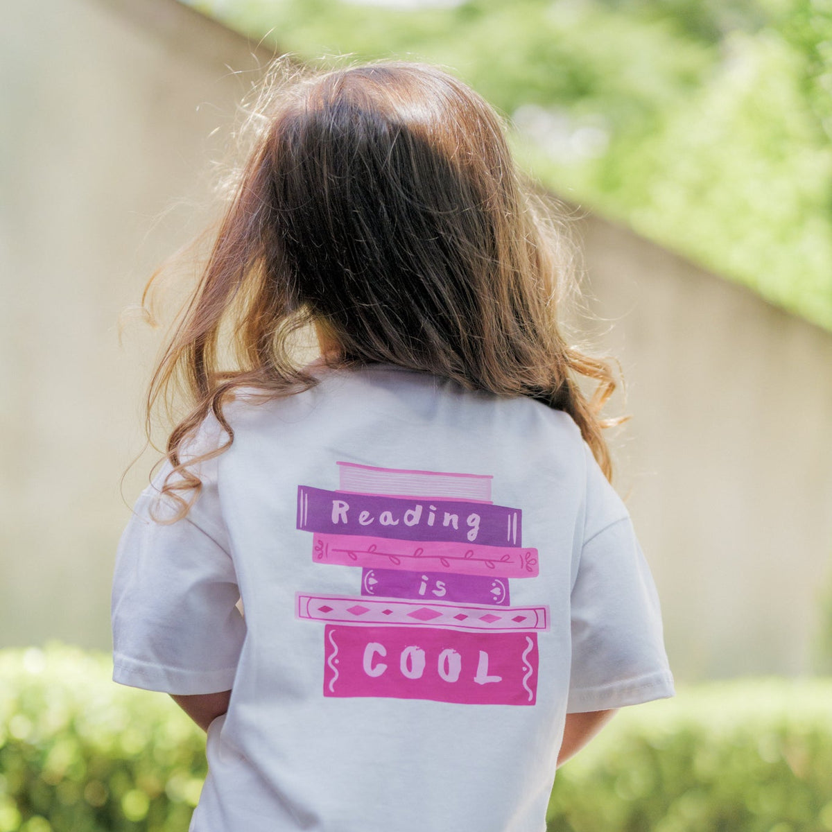Child wearing a shirt with 'Reading is Cool' text outdoors.