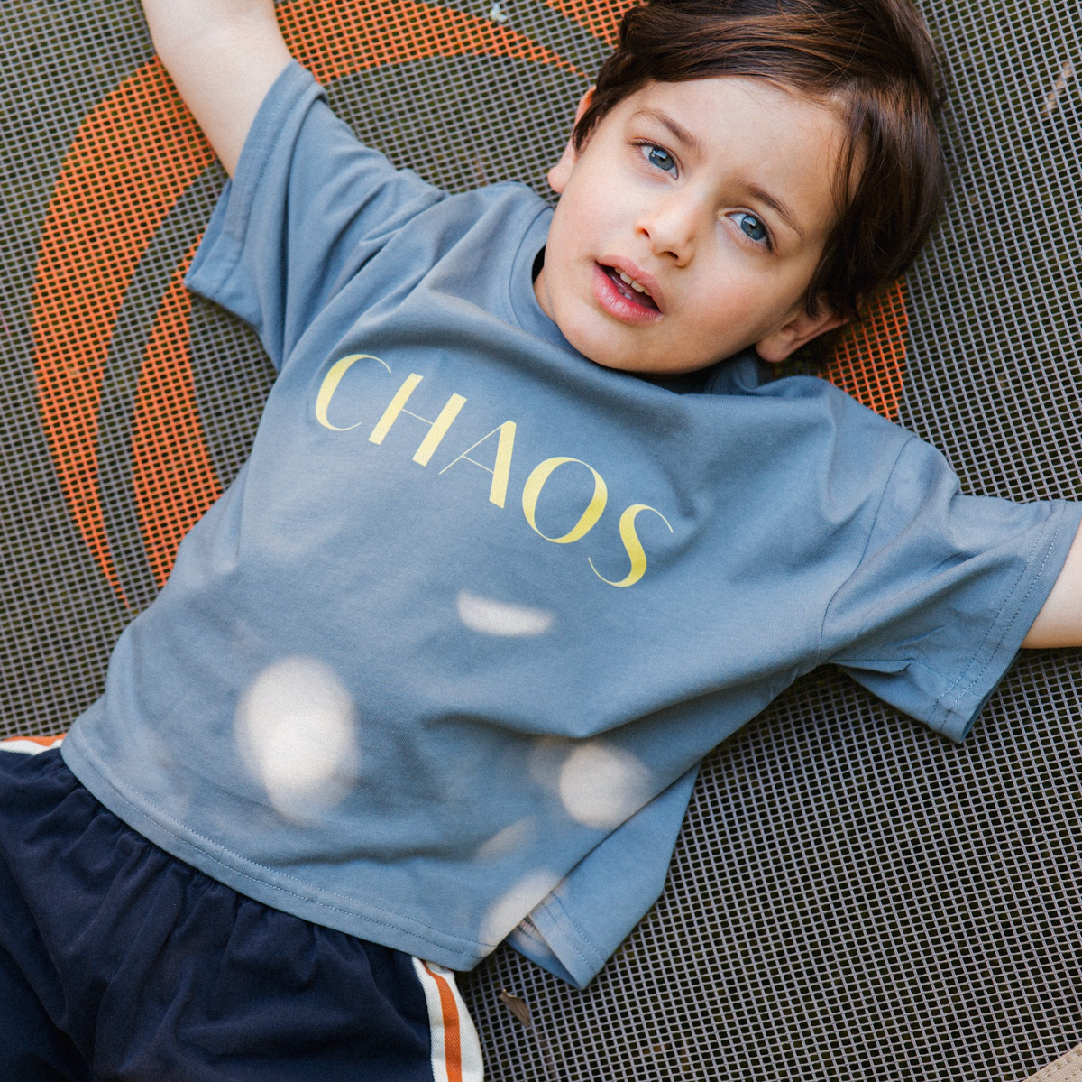 Child wearing a blue t-shirt with 'CHAOS' printed on it, lying on a textured surface.