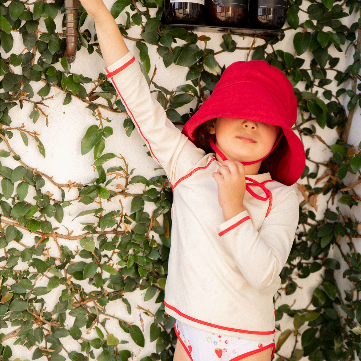 Child wearing a white outfit with red trim and a red hat against a leafy background