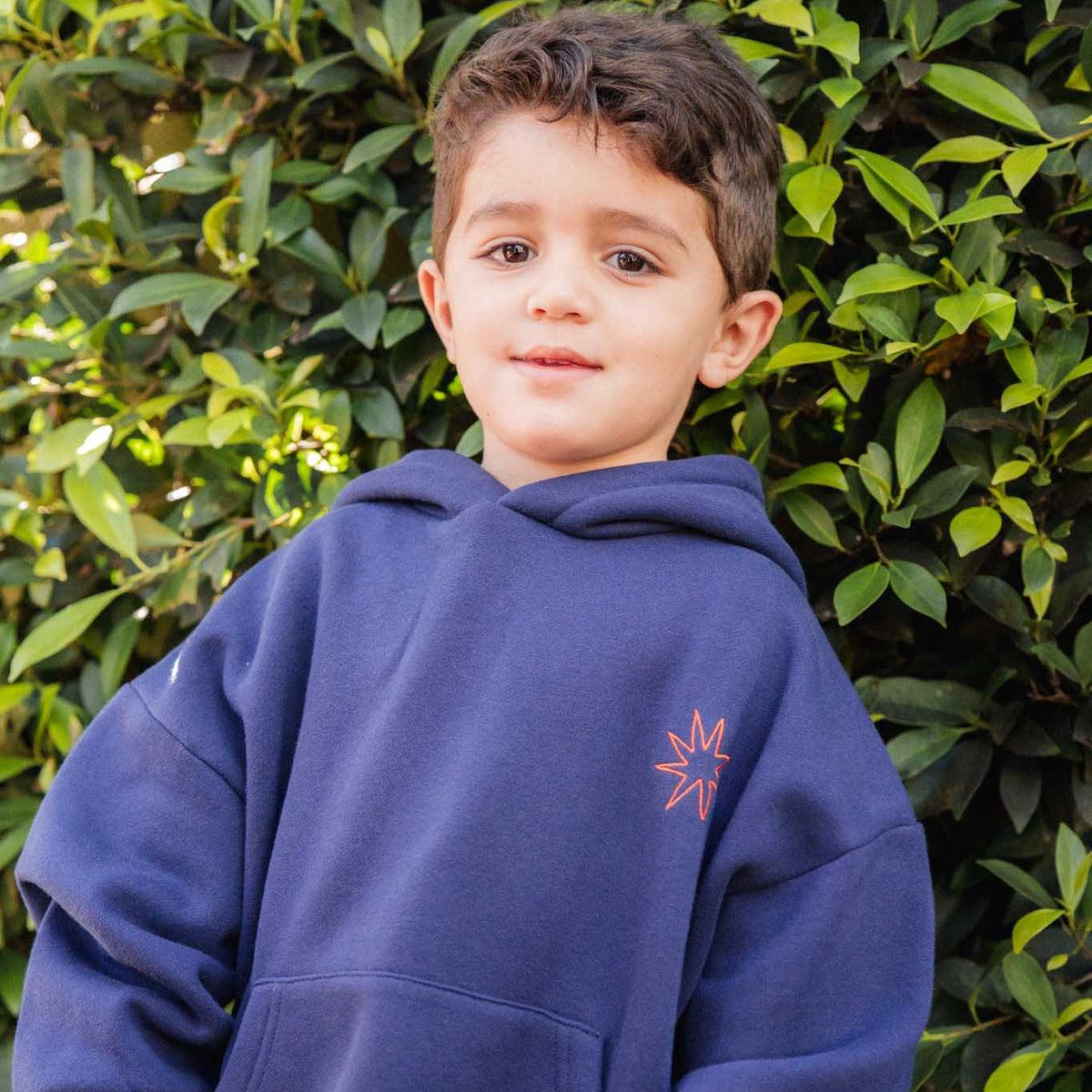 Child wearing a blue hoodie with a logo in front of green foliage