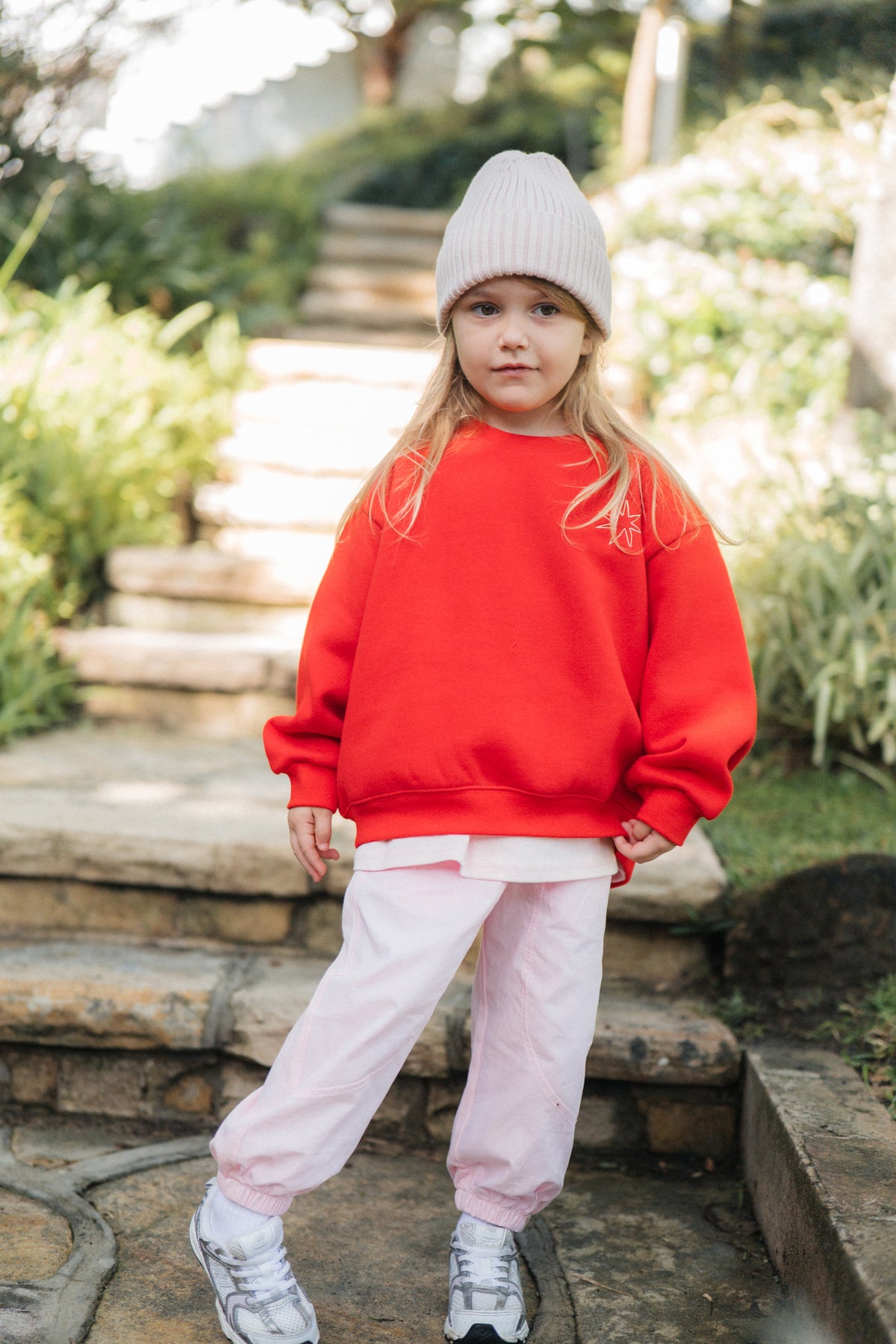 Child wearing a red sweatshirt and pink pants standing on stone steps outdoors.