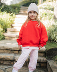 Child wearing a red sweatshirt and pink pants standing on stone steps outdoors.